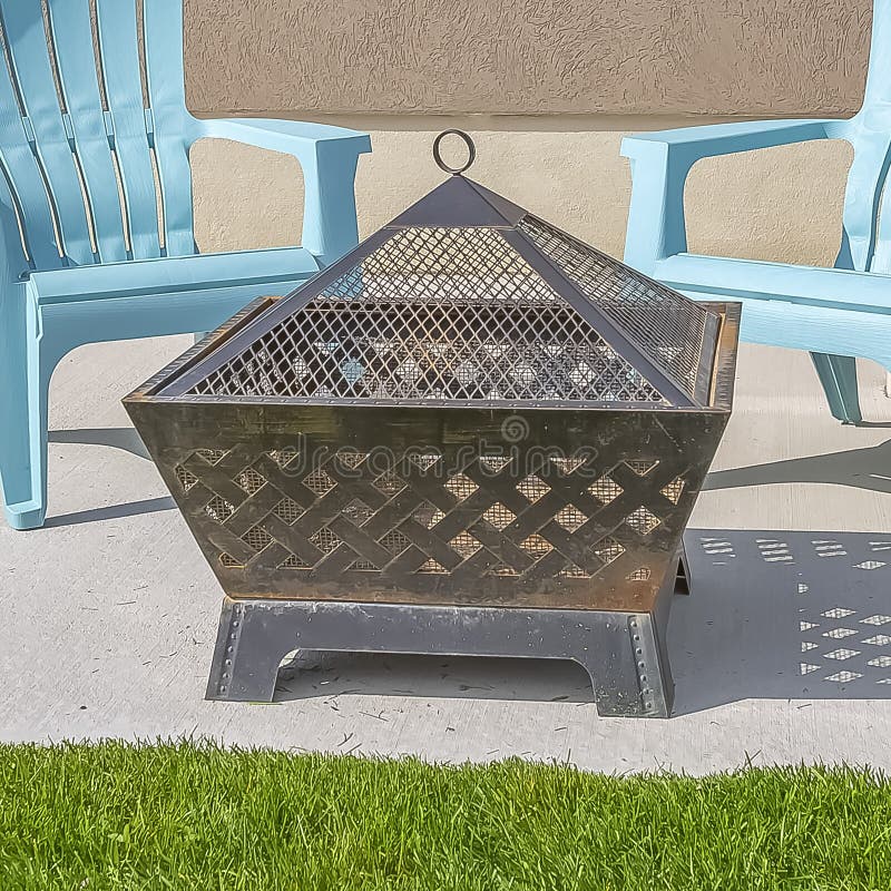 Square frame Square fire pit and blue plastic chairs on the yard of a home on a sunny day