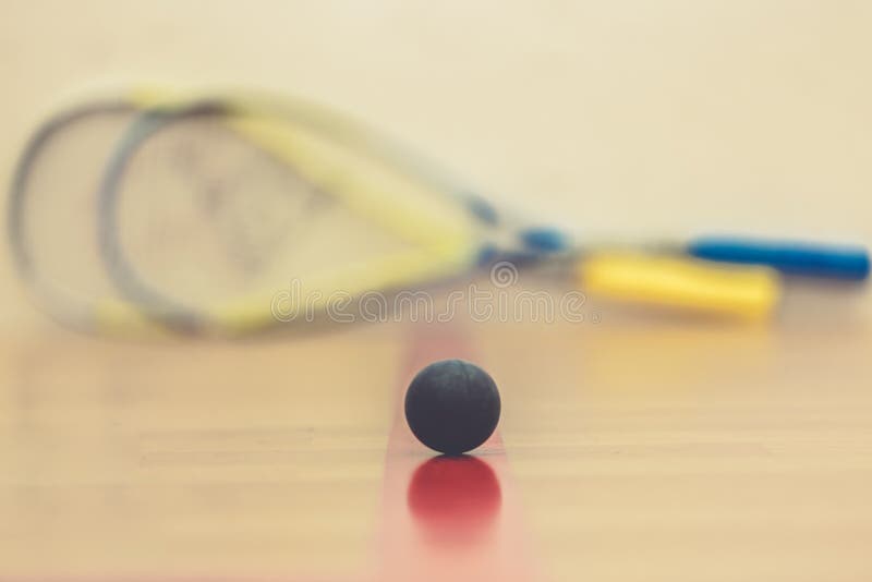 Squash ball on court with two squash rockets ready to play
