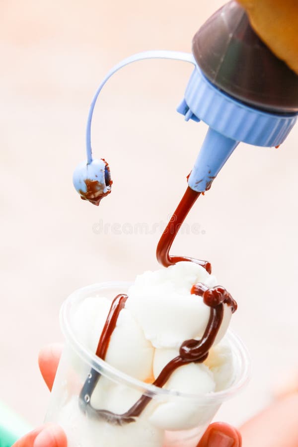 Squeeze Chocolate from a Bottle into Ice Cream in the Cup. Stock Image