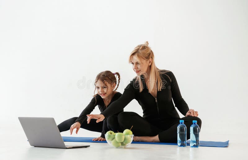Srebrne jabłka do laptopów i woda. Matka i mała córka są w ubraniu fitness na matce jogi fotografia stock