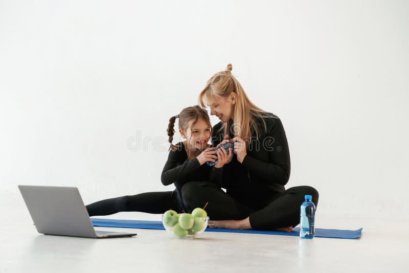 Srebrne jabłka do laptopów i woda. Matka i mała córka są w ubraniu fitness na matce jogi zdjęcia stock