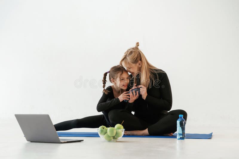 Srebrne jabłka do laptopów i woda. Matka i mała córka są w ubraniu fitness na matce jogi fotografia stock