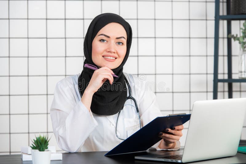 St?ende av att le den muslimska kvinnliga doktorn p? hennes kontor royaltyfri bild St?ende av att le den muslimska kvinnliga doktorn p? hennes kontor royaltyfri bild