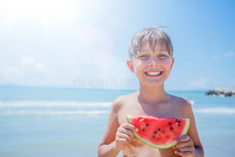 St? ende av den f? rtjusande pojken med vattenmelon p? stranden royaltyfria bilder