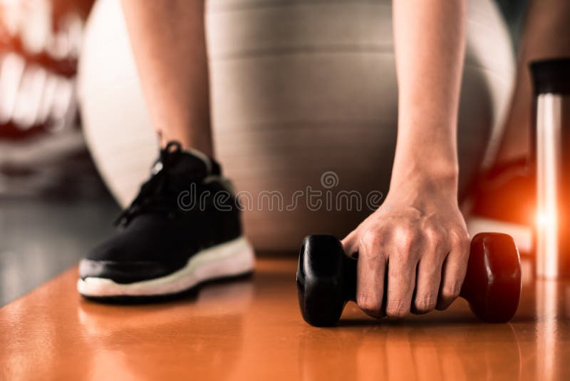 St?ng sig upp av sportkvinnan som sitter p? yogaboll och hastigt grepphantel p? golv vid handen i bakgrund f?r mitt f?r kondition