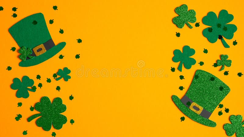 St. Patricks Day frame of shamrock leaf clovers, Irish elf hats and confetti on orange background. Flat lay, top view. Saint Patrick`s Day greeting card template, poster design, banner mockup