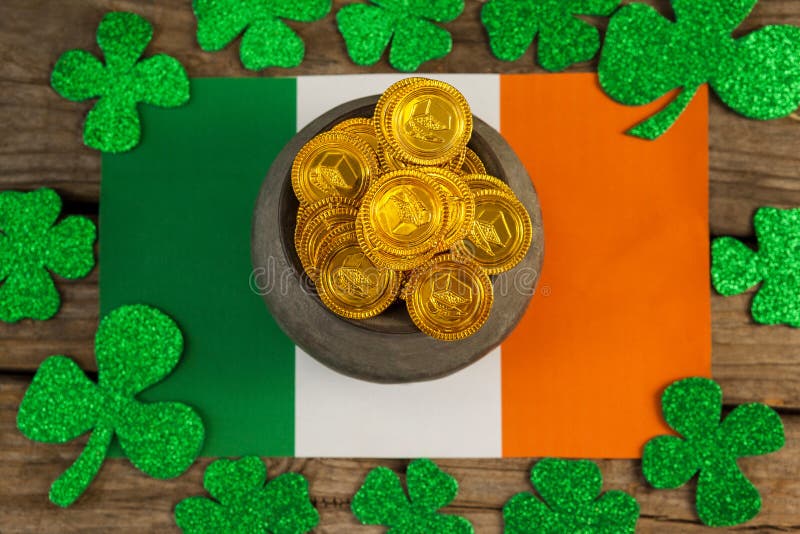 St. Patricks Day pot of chocolate gold coins and irish flag surrounded by shamrock on wooden table