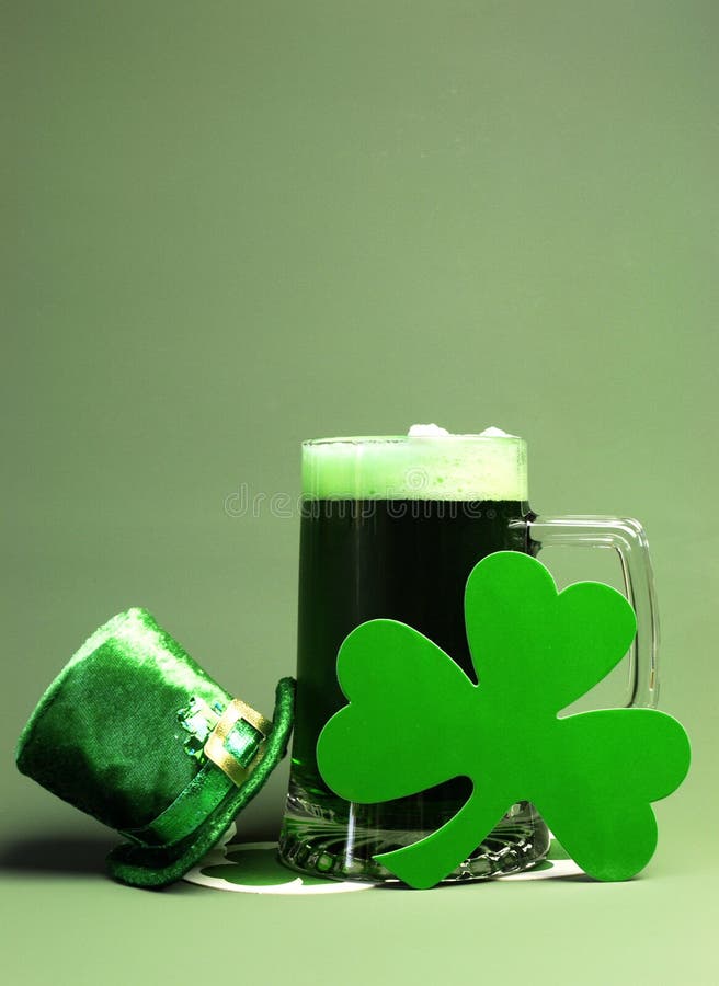 Celebrate all the fun and luck of the Irish of St Patrick's Day with a glass stein of green beer, a large shamrock and leprechaun hat on a green background. Vertical with copy space for your text here. Celebrate all the fun and luck of the Irish of St Patrick's Day with a glass stein of green beer, a large shamrock and leprechaun hat on a green background. Vertical with copy space for your text here.