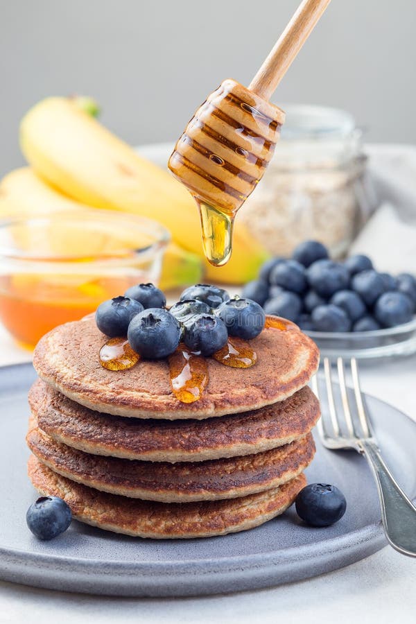 Stack av friska vindrutor av havremjölsbananer som är täckta med blåbär och honung, honung som flödar ned från honungsdippar elle arkivfoto Stack av friska vindrutor av havremjölsbananer som är täckta med blåbär och honung, honung som flödar ned från honungsdippar elle arkivfoto