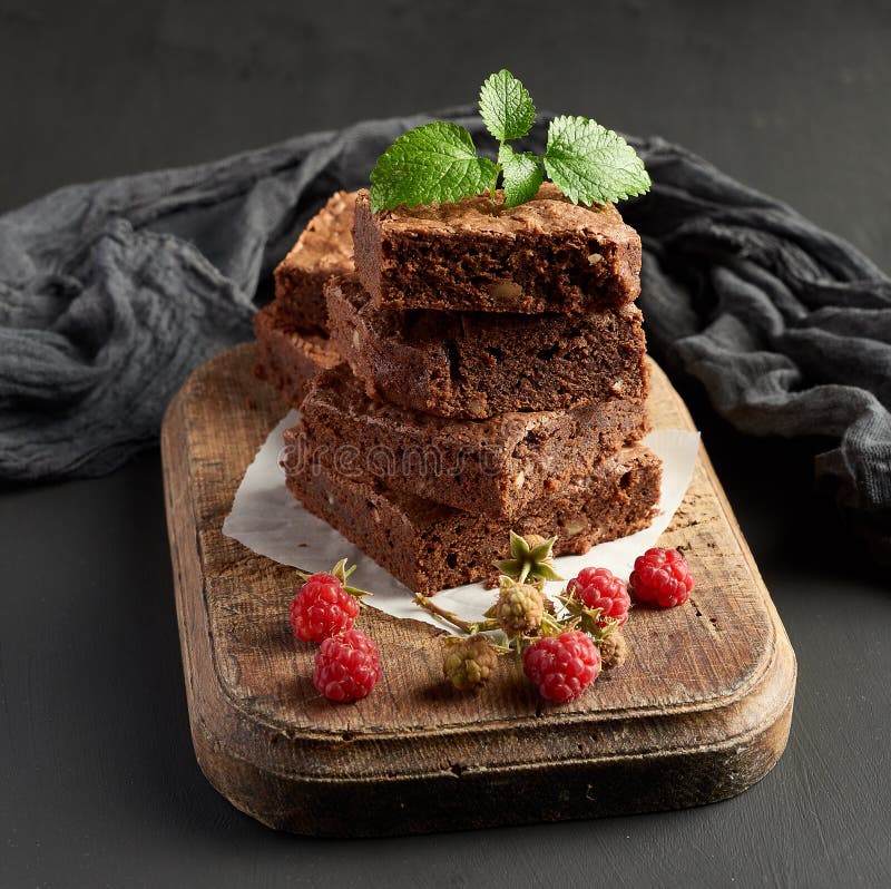 stack of baked square pieces of chocolate brownie cake on brown wooden cutting board