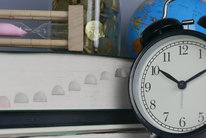 Stack of book with hourglass,globe,jar of coins, and clock. Money,time,world and education concept