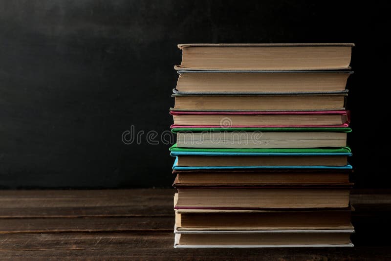 A stack of books on a brown wooden table and on a black background. Old books. Education. study With space for inscription