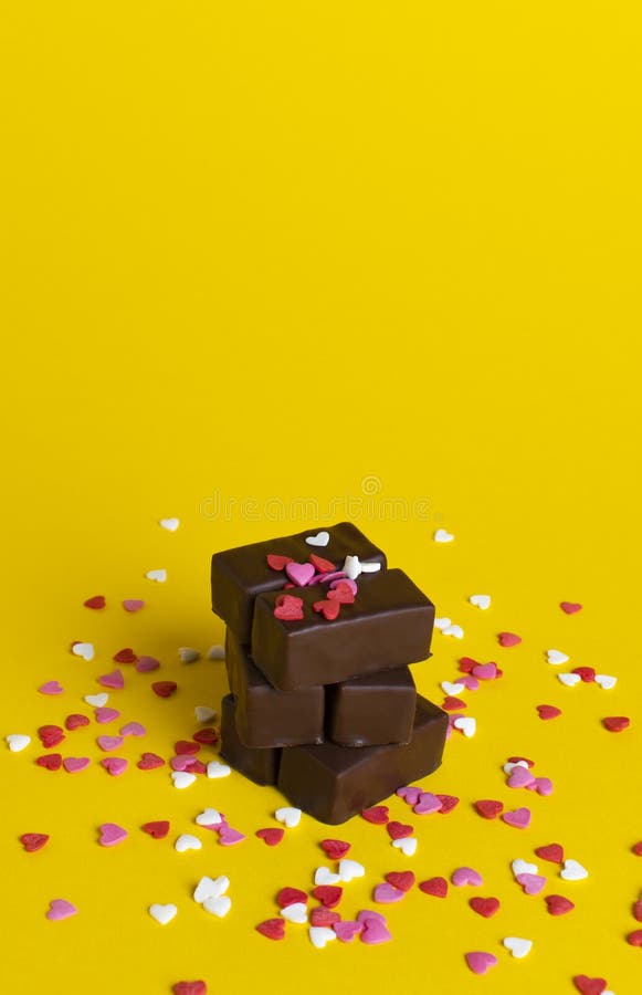 A stack of chocolates on a background of confetti from small hearts. yellow background