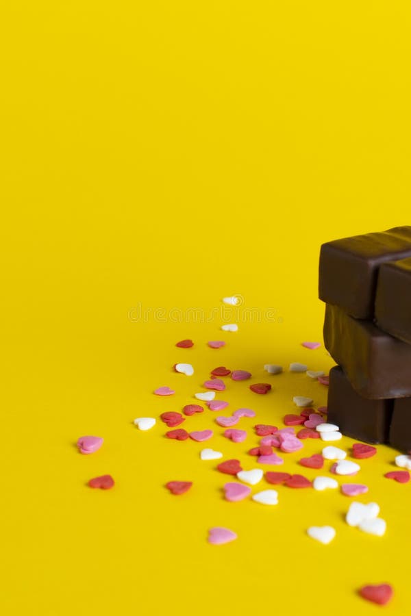 A stack of chocolates on a background of confetti from small hearts. yellow background
