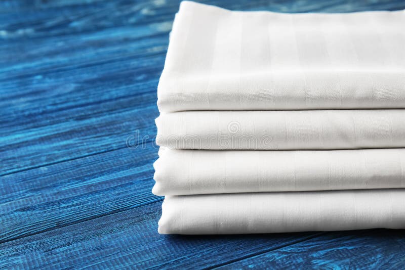 Stack of clean bed sheets on color wooden background, closeup