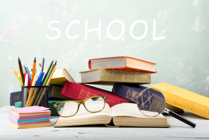 stack of color books, eyeglasses, stationery and magnifying glass on a table and text & x22;School& x22; on green background