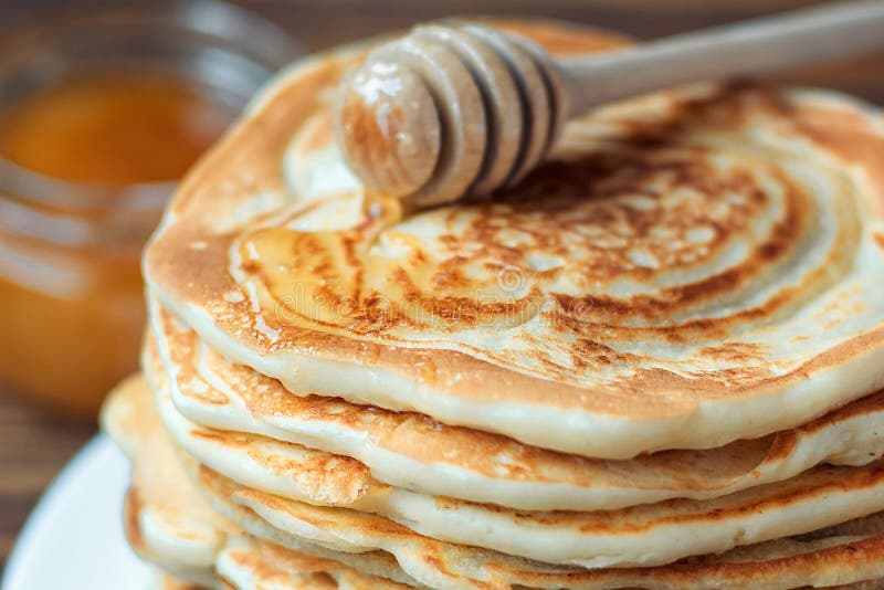 Stack of delicious, homemade pancakes with honey on white plate on wooden background. Healthy breakfast, close up. Pancake`s Day. Closeup, butter.