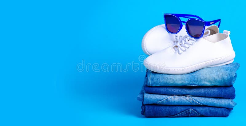 Stack folded jeans and sunglasses, white sneakers stock photo