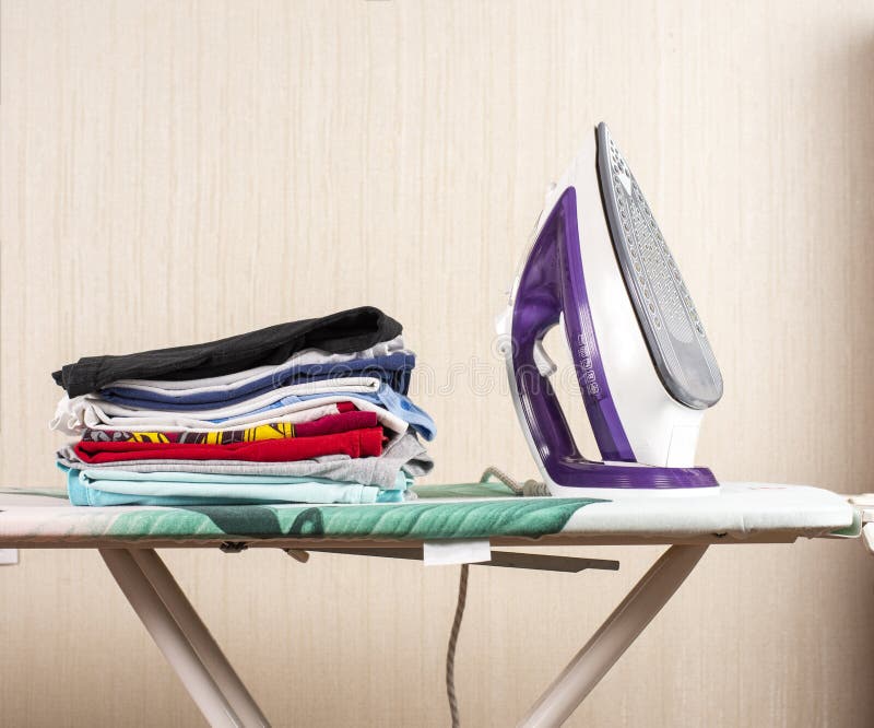 A Stack of Ironed Laundry on the Ironing Board Next To the Iron Stock