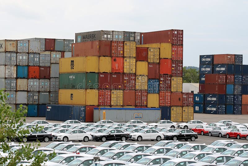 Italy - Month 09.2015: Rows of new beautiful audi cars near stack of metal cargo containers of different leading shipping companies containerized goods international delivery outdoor, horizontal