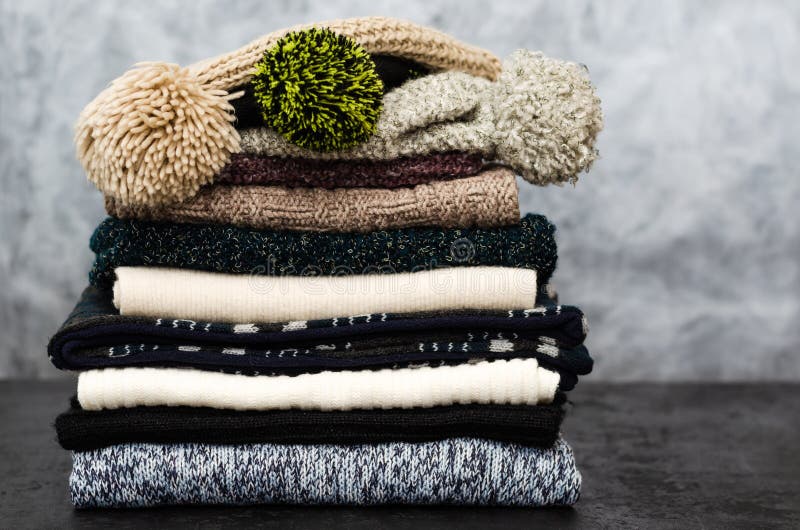 A stack of neatly folded knitted winter scarves and hats on gray background. Closeup. Season of warm clothes