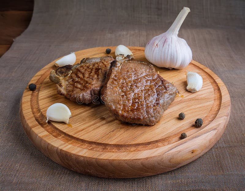 Fried steak pieces on a wooden board and garlics stock illustration