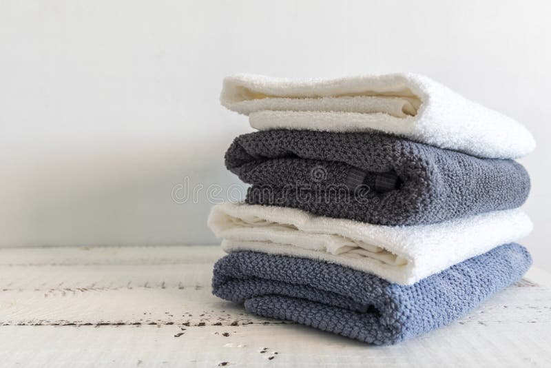 A stack of white and grey bath towels on white wooden table. Spa and wellness, cotton terry textile.