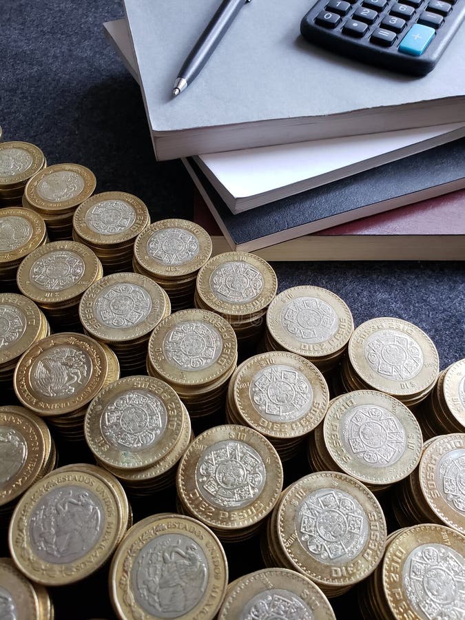 stacked books, calculator, pen and mexican coins of ten pesos