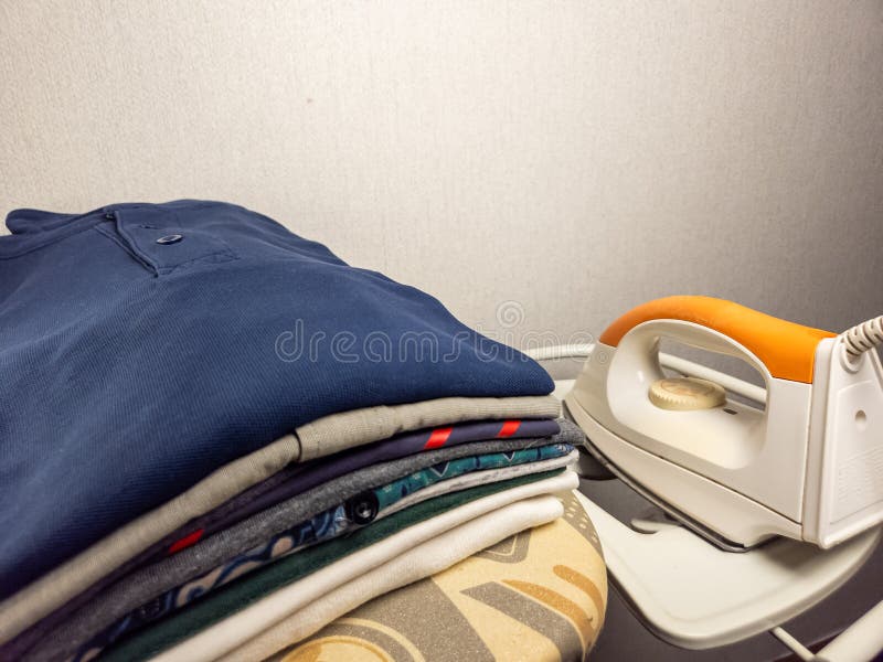 Stacked neatly folded clothes with an iron on ironing board stock image