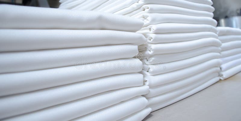 Stacks of folded white fabrics or sheets in an industrial laundry