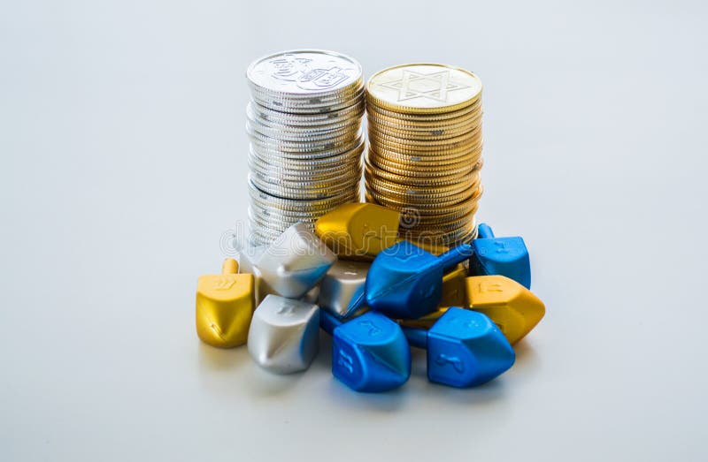 2 stacks of gold and silver Hanukkah coins surrounded by tiny dreidels isolated on a solid background. 2 stacks of gold and silver Hanukkah coins surrounded by tiny dreidels isolated on a solid background