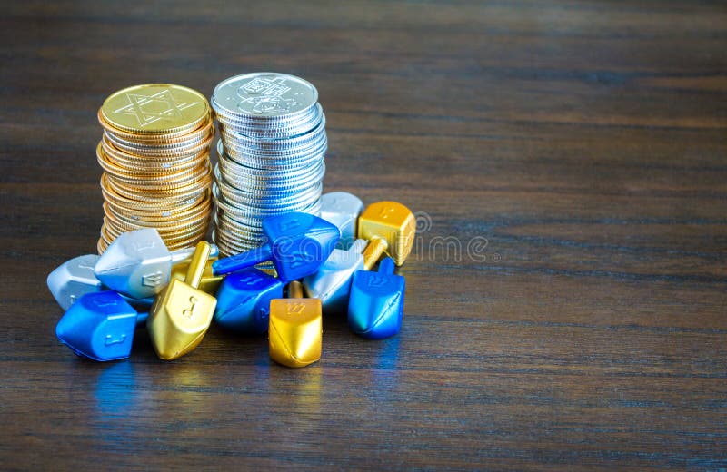 2 stacks of gold and silver Hanukkah coins surrounded by tiny dreidels on a wooden table with copy space. 2 stacks of gold and silver Hanukkah coins surrounded by tiny dreidels on a wooden table with copy space