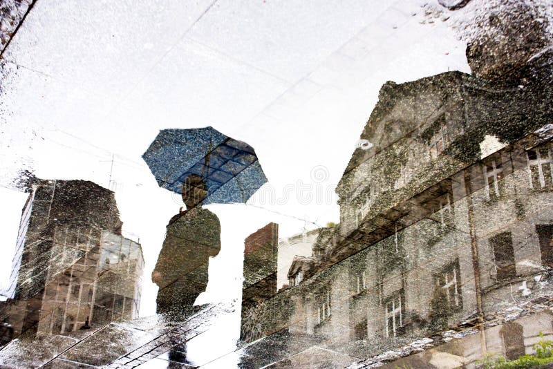 Reflection shadow silhouette of a person under umbrella and a building in the puddle. Reflection shadow silhouette of a person under umbrella and a building in the puddle