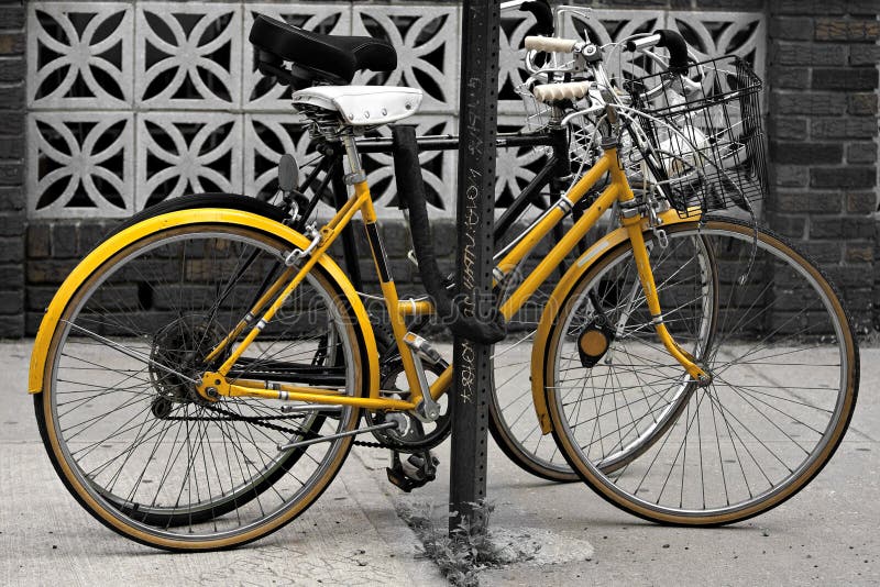 A couple of bicycles chained to a post in the city. Selective color with highlight on the yellow. A couple of bicycles chained to a post in the city. Selective color with highlight on the yellow.