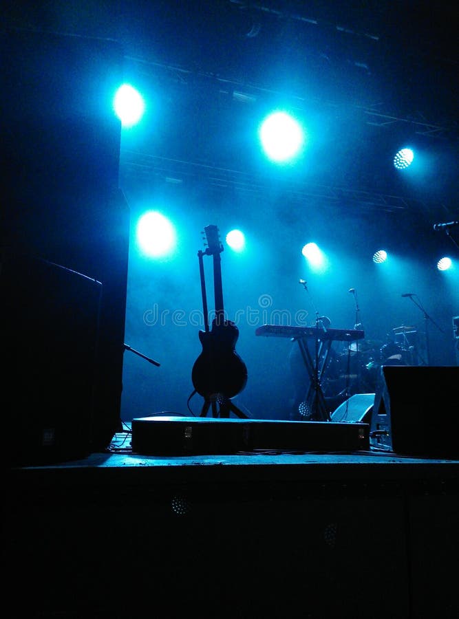 Stage with black silouette of standing guitar with microphones and other musical instruments under blue spotlights lighting down