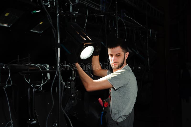 The stage worker sets up the lights. Male, equipment.