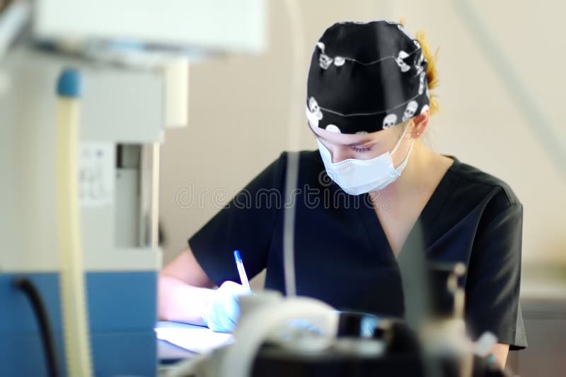 Intern surgeon records the progress of the operating room in a journal. Wearing an operating gown the anesthesiologist describes the operation in a document. Intern surgeon records the progress of the operating room in a journal. Wearing an operating gown the anesthesiologist describes the operation in a document