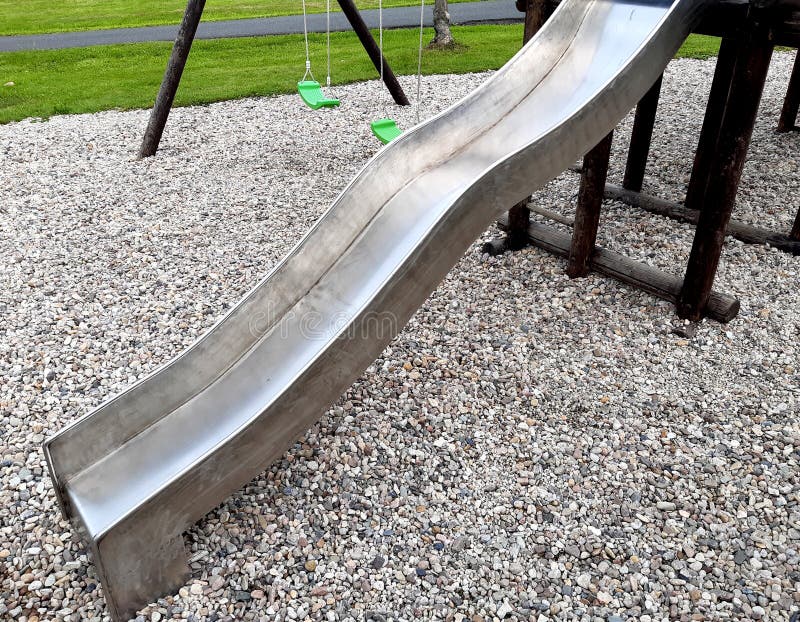 Stainless steel slide and swings on the playground in the park in gray pebbles