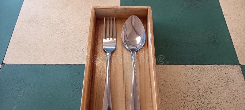 Stainless steel spoon and fork in wooden tray cutlery box on checkered tile, ideal for minimalist restaurants stock photos