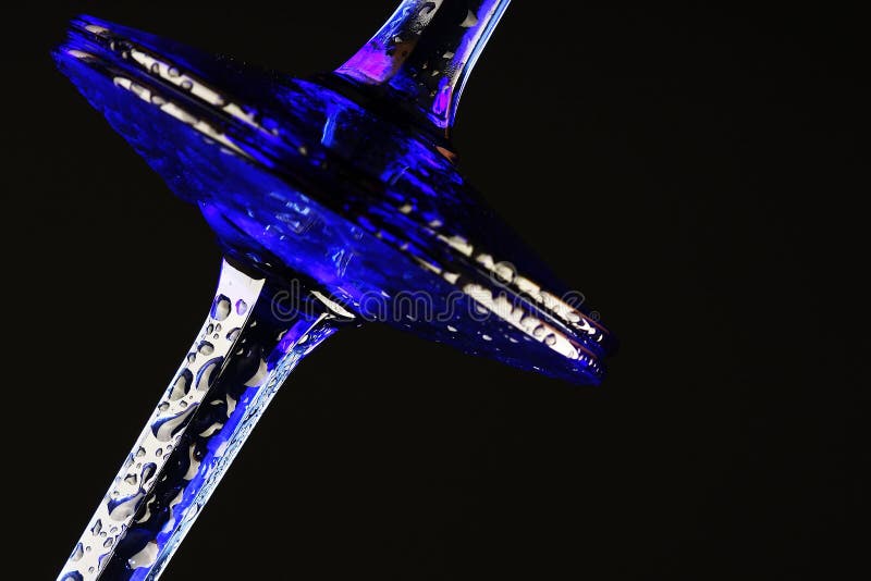 Stems and base of 2 blue champagne flutes?glasses. They have condensation drops..shot on black background. Stems and base of 2 blue champagne flutes?glasses. They have condensation drops..shot on black background