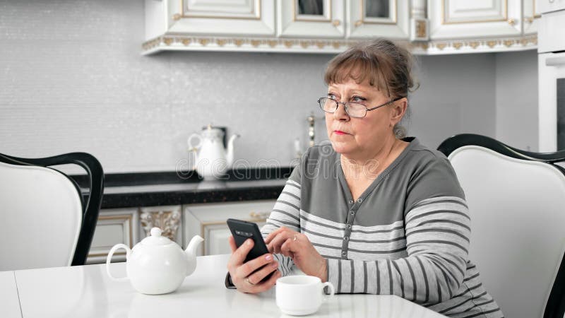 Stamvrouw in bril met smartphone bij keuken binnenshuis