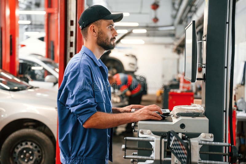 Standing by Computer Terminal. Auto Mechanic Working in Garage Stock