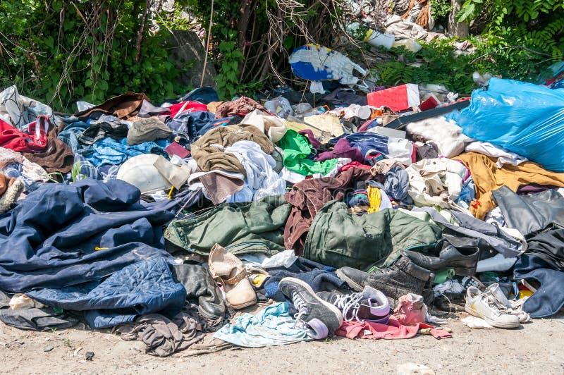 Pile of old clothes and shoes dumped on the grass as junk and garbage, littering and polluting the environment. Pile of old clothes and shoes dumped on the grass as junk and garbage, littering and polluting the environment.