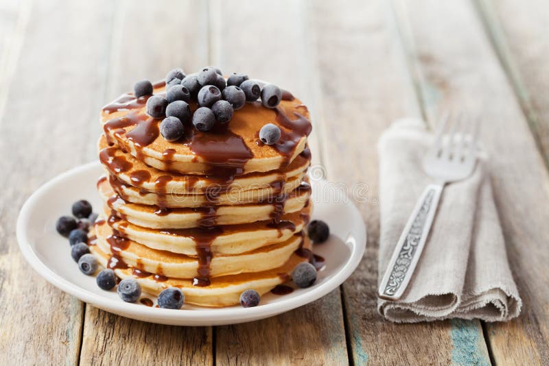 Stapel gebackene Pfannkuchen oder Stückchen mit Schokoladensoße und gefrorenen Blaubeeren in einer weißen Platte lizenzfreies stockfoto Stapel gebackene Pfannkuchen oder Stückchen mit Schokoladensoße und gefrorenen Blaubeeren in einer weißen Platte lizenzfreies stockfoto