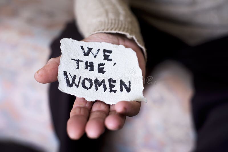 Closeup of an old caucasian woman indoors with a piece of paper in her hand with the text we the women written in it. Closeup of an old caucasian woman indoors with a piece of paper in her hand with the text we the women written in it