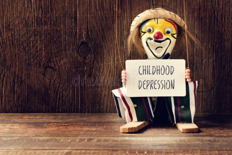 Closeup of an old marionette with its face painted as a sad clown holding a signboard with the text childhood depression. Closeup of an old marionette with its face painted as a sad clown holding a signboard with the text childhood depression