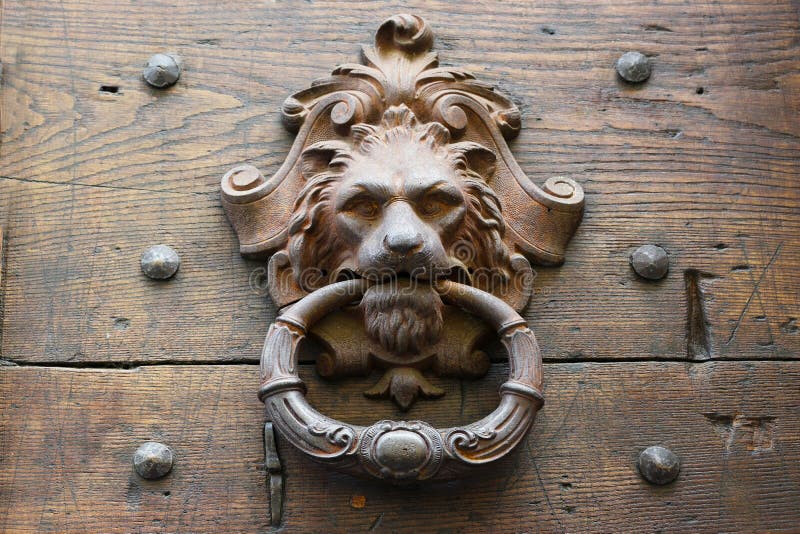 Starego metalu drzwiowy knocker jako lwy przewodzi na nieociosanym drewnianym drzwi w Italy zdjęcie stock Starego metalu drzwiowy knocker jako lwy przewodzi na nieociosanym drewnianym drzwi w Italy zdjęcie stock
