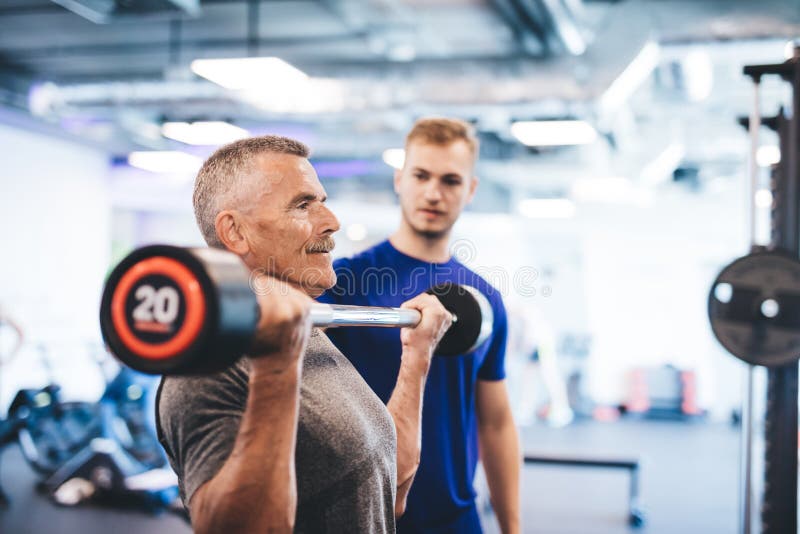 Starego mężczyzna udźwigu ciężary, doglądający gym asystentem zdjęcie royalty free Starego mężczyzna udźwigu ciężary, doglądający gym asystentem zdjęcie royalty free