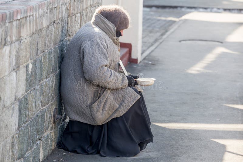 Russia, Vladivostok, 02/10/2018. Elderly poor woman begging alms in the street in a cold winter day. Poverty and poor people. Beggars on the streets of the city. Social problems concept. Russia, Vladivostok, 02/10/2018. Elderly poor woman begging alms in the street in a cold winter day. Poverty and poor people. Beggars on the streets of the city. Social problems concept