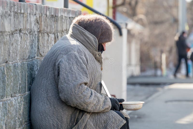 Russia, Vladivostok, 02/10/2018. Elderly poor woman begging alms in the street in a cold winter day. Poverty and poor people. Beggars on the streets of the city. Social problems concept. Russia, Vladivostok, 02/10/2018. Elderly poor woman begging alms in the street in a cold winter day. Poverty and poor people. Beggars on the streets of the city. Social problems concept